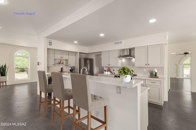 kitchen with a kitchen breakfast bar, light countertops, freestanding refrigerator, decorative backsplash, and wall chimney exhaust hood