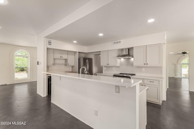 kitchen featuring stainless steel appliances, backsplash, light countertops, and wall chimney range hood