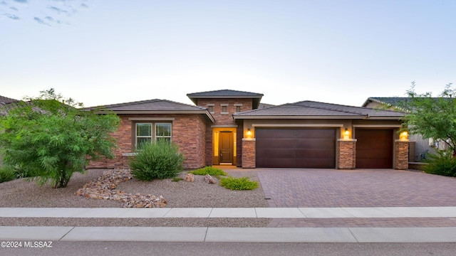 prairie-style home featuring a garage, stone siding, and decorative driveway