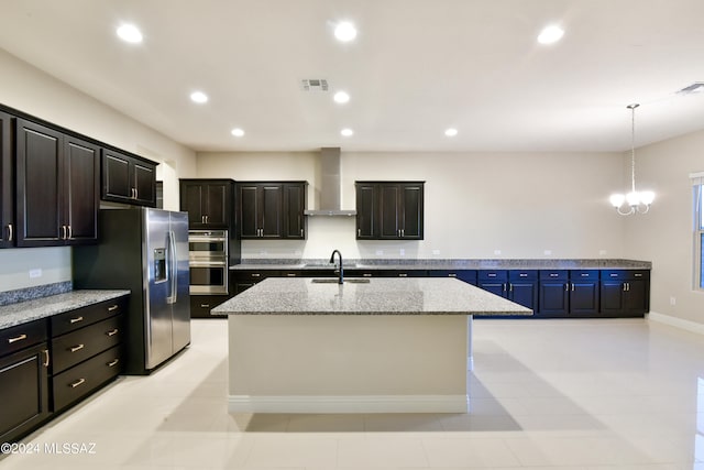 kitchen featuring a center island with sink, appliances with stainless steel finishes, wall chimney range hood, a sink, and recessed lighting