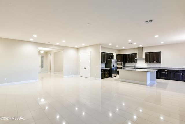 kitchen featuring stainless steel appliances, wall chimney exhaust hood, light tile patterned floors, and a kitchen island with sink