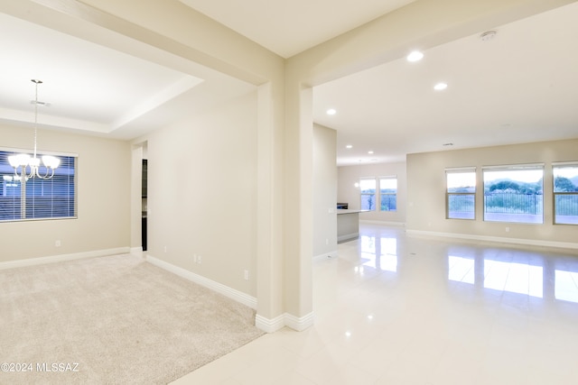 empty room featuring a tray ceiling, recessed lighting, light carpet, a chandelier, and baseboards