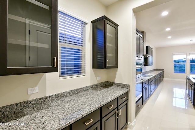 kitchen featuring light tile patterned flooring, stainless steel oven, dark brown cabinets, and light stone counters