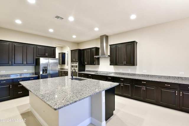 kitchen featuring stainless steel refrigerator with ice dispenser, visible vents, a kitchen island with sink, a sink, and wall chimney range hood