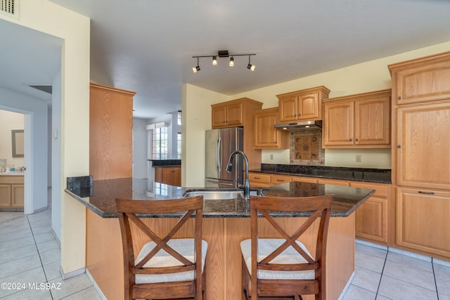 kitchen with sink, light tile patterned floors, stainless steel refrigerator, a breakfast bar area, and dark stone counters