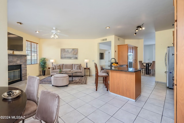 kitchen featuring appliances with stainless steel finishes, a stone fireplace, kitchen peninsula, light tile patterned floors, and ceiling fan