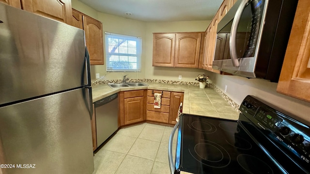 kitchen featuring tile countertops, sink, light tile patterned floors, and appliances with stainless steel finishes