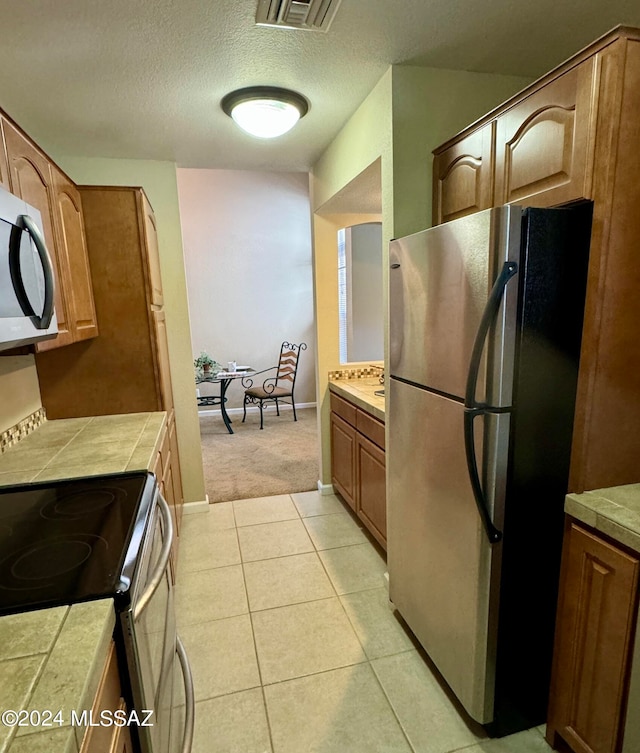 kitchen with tile countertops, appliances with stainless steel finishes, light colored carpet, and a textured ceiling