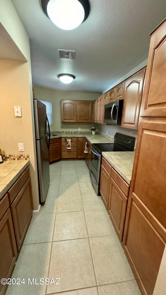 kitchen with appliances with stainless steel finishes, a textured ceiling, light tile patterned floors, and tile counters