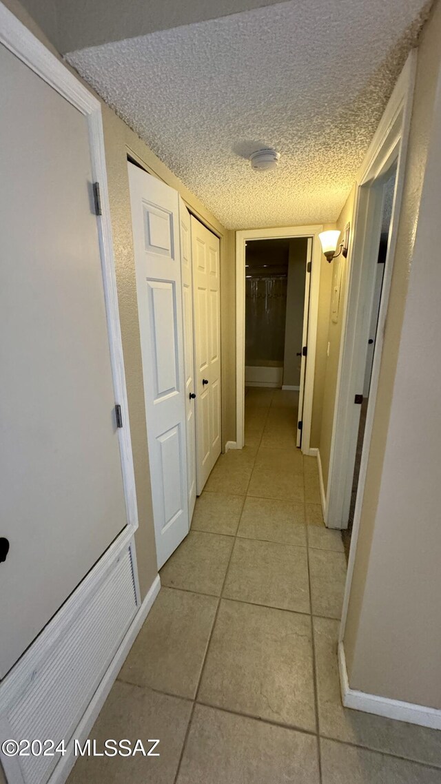 hallway with a textured ceiling and light tile patterned floors