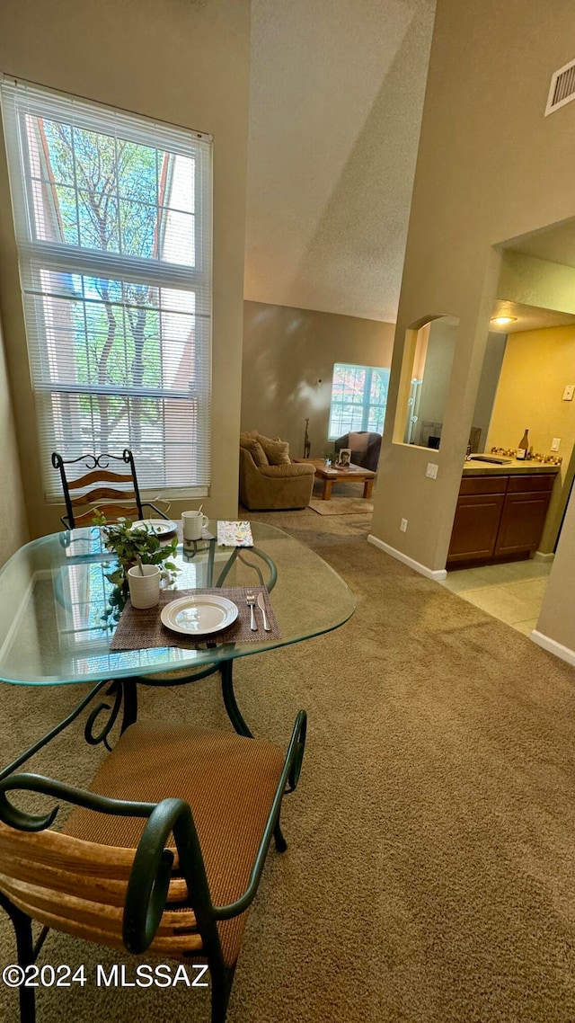 dining room with a textured ceiling, high vaulted ceiling, and light colored carpet