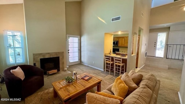 living room with a high ceiling, a tiled fireplace, and light carpet