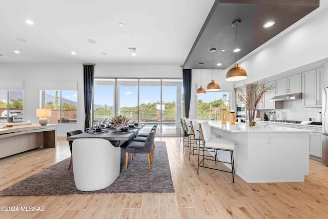 kitchen featuring light wood-type flooring, backsplash, an island with sink, hanging light fixtures, and a breakfast bar area