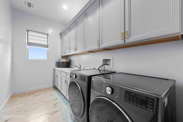 laundry room with light hardwood / wood-style flooring, cabinets, washing machine and clothes dryer, and sink