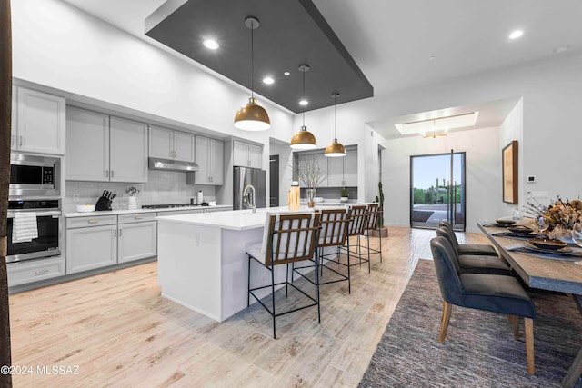 kitchen featuring pendant lighting, light hardwood / wood-style floors, a kitchen island with sink, a breakfast bar, and stainless steel appliances