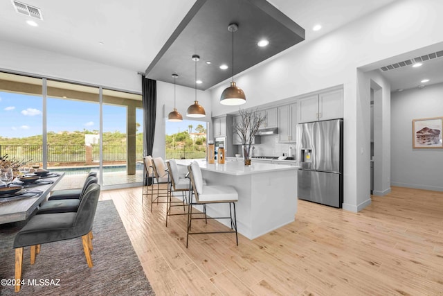 kitchen with gray cabinetry, light wood-type flooring, pendant lighting, stainless steel fridge with ice dispenser, and a kitchen island with sink