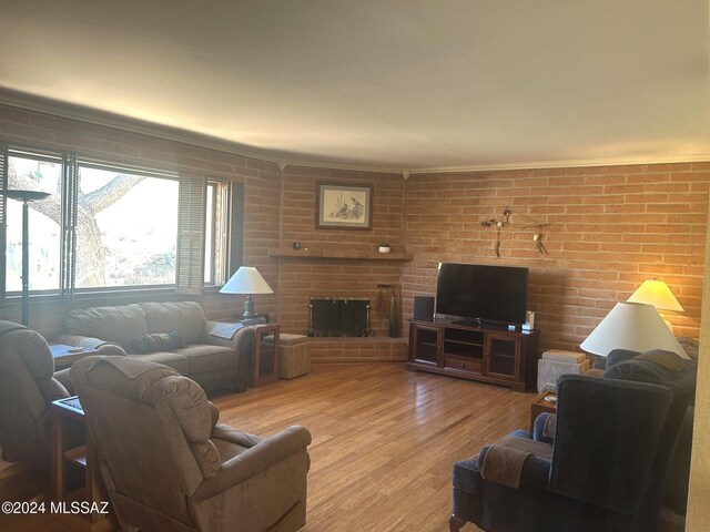 living room featuring crown molding, brick wall, light wood-type flooring, and a fireplace