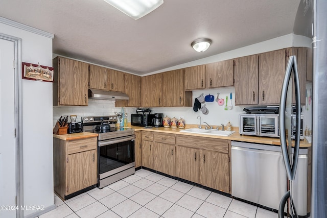 kitchen featuring backsplash, appliances with stainless steel finishes, sink, light tile patterned flooring, and a textured ceiling