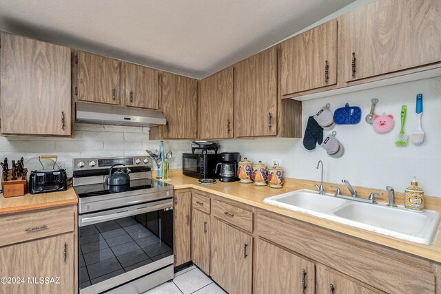 kitchen featuring light tile patterned floors, tasteful backsplash, stainless steel range with electric cooktop, and sink