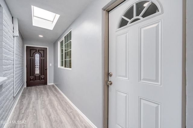 corridor featuring brick wall, light hardwood / wood-style floors, and a skylight