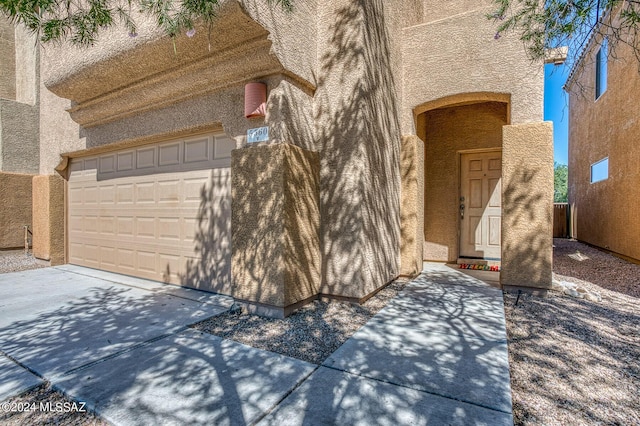 doorway to property with a garage, driveway, and stucco siding