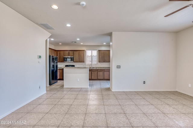 kitchen featuring ceiling fan, black fridge, light tile patterned floors, sink, and a center island