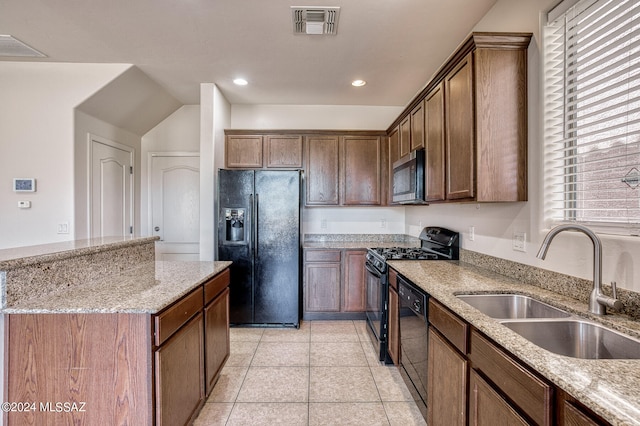 kitchen featuring light stone counters, light tile patterned floors, sink, black appliances, and a center island