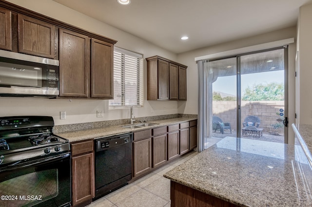 kitchen featuring light tile patterned flooring, dark brown cabinetry, sink, light stone counters, and black appliances