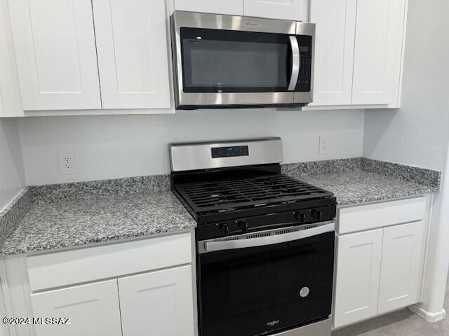 kitchen with appliances with stainless steel finishes, white cabinetry, light stone counters, and light tile patterned floors