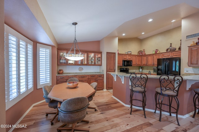 kitchen featuring black appliances, a kitchen breakfast bar, light hardwood / wood-style flooring, vaulted ceiling, and light stone counters