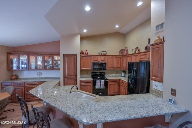 kitchen featuring sink, a kitchen breakfast bar, kitchen peninsula, vaulted ceiling, and black appliances