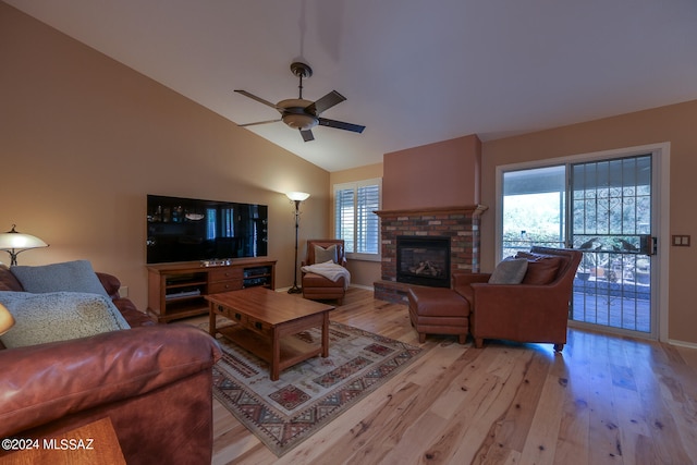 living room featuring a brick fireplace, plenty of natural light, vaulted ceiling, and light hardwood / wood-style flooring