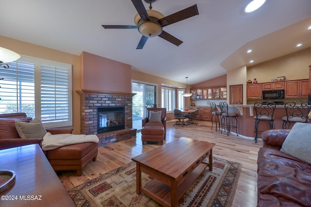 living room featuring a brick fireplace, vaulted ceiling, light hardwood / wood-style flooring, and ceiling fan