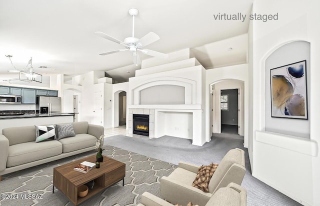 carpeted living room featuring a tiled fireplace and ceiling fan with notable chandelier