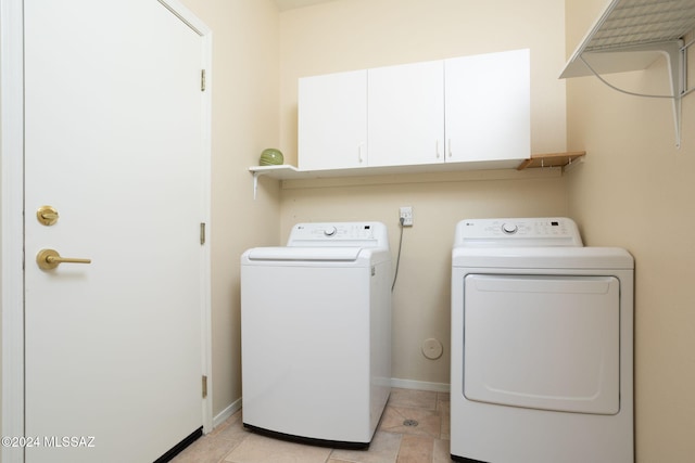 laundry room featuring washing machine and clothes dryer, light tile patterned flooring, and cabinets