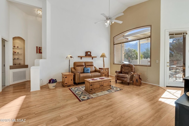 sitting room featuring built in shelves, light hardwood / wood-style flooring, high vaulted ceiling, and ceiling fan