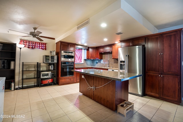 kitchen featuring dark stone countertops, stainless steel appliances, ceiling fan, a kitchen island, and decorative backsplash