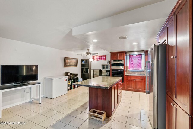 kitchen featuring ceiling fan, reddish brown cabinets, dark stone countertops, appliances with stainless steel finishes, and light tile patterned floors
