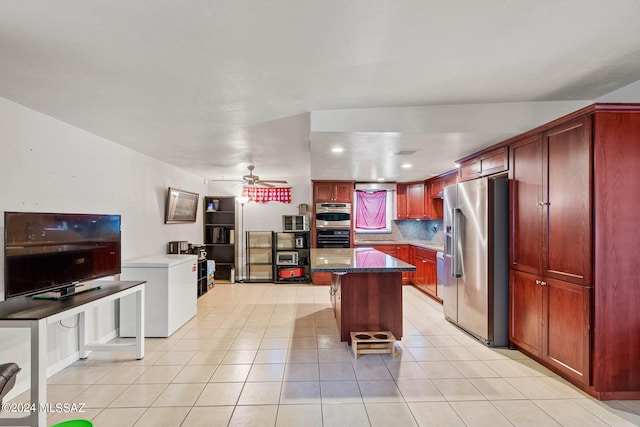 kitchen featuring appliances with stainless steel finishes, dark stone counters, ceiling fan, a kitchen island, and tasteful backsplash