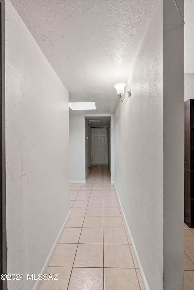 corridor with baseboards, a textured ceiling, and light tile patterned flooring
