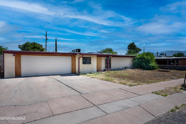 ranch-style house with central air condition unit, an attached garage, concrete driveway, and stucco siding