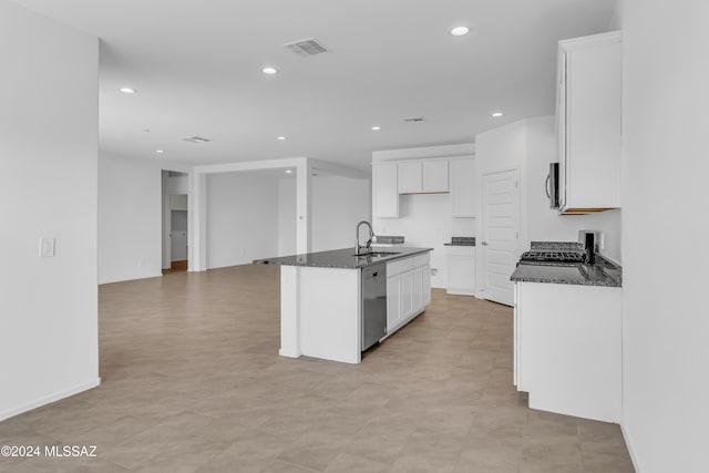 kitchen featuring dark stone countertops, white cabinetry, an island with sink, and appliances with stainless steel finishes