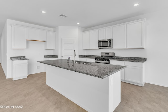 kitchen with dark stone counters, sink, an island with sink, appliances with stainless steel finishes, and white cabinetry