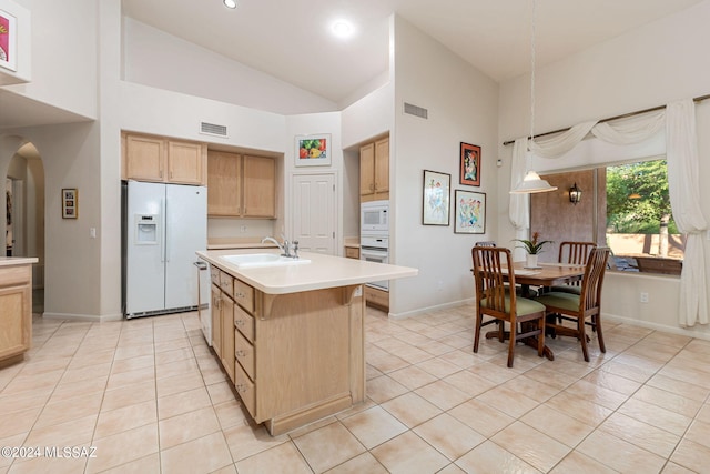 kitchen with decorative light fixtures, white appliances, a center island with sink, sink, and high vaulted ceiling