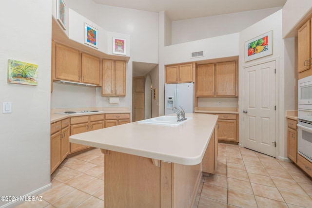 kitchen featuring vaulted ceiling, white appliances, light tile patterned floors, an island with sink, and a kitchen bar