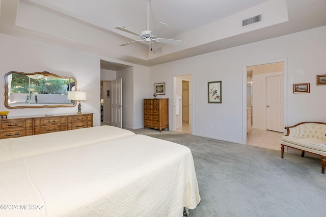 carpeted bedroom with a raised ceiling, connected bathroom, and ceiling fan