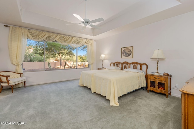 carpeted bedroom with ceiling fan and a raised ceiling