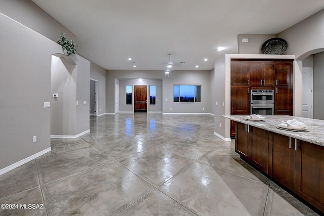 kitchen featuring dark brown cabinetry, light stone counters, and stainless steel double oven