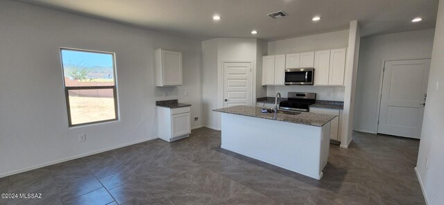 kitchen with white cabinets, appliances with stainless steel finishes, dark stone counters, and a kitchen island with sink