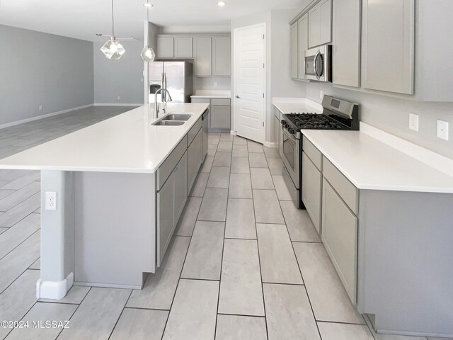 kitchen with gray cabinets, stainless steel appliances, sink, and a center island with sink